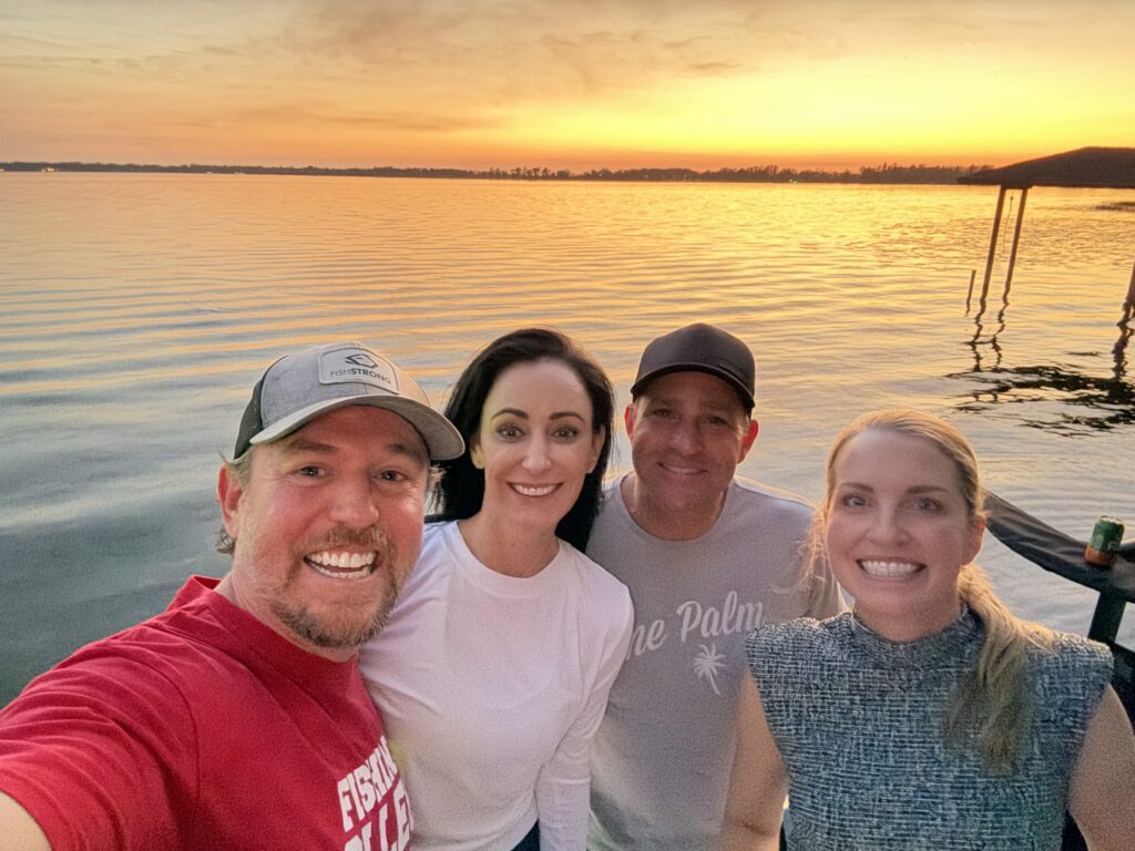 Three women relaxing on a giant inflatable flamingo float on a Winter Haven lake, with a dock and lakefront home behind them